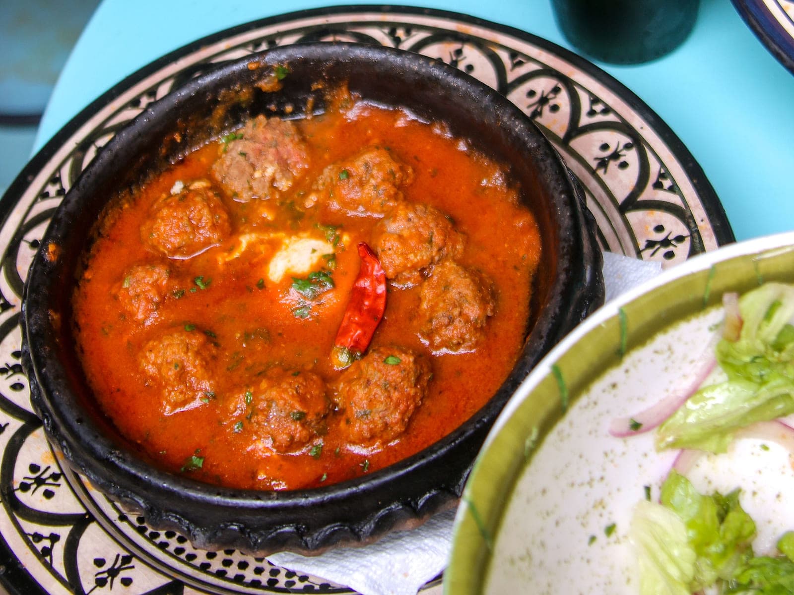 Moroccan kefta mkaouara — beef meatballs in red tomato sauce with eggs set on top, in a clay tagine